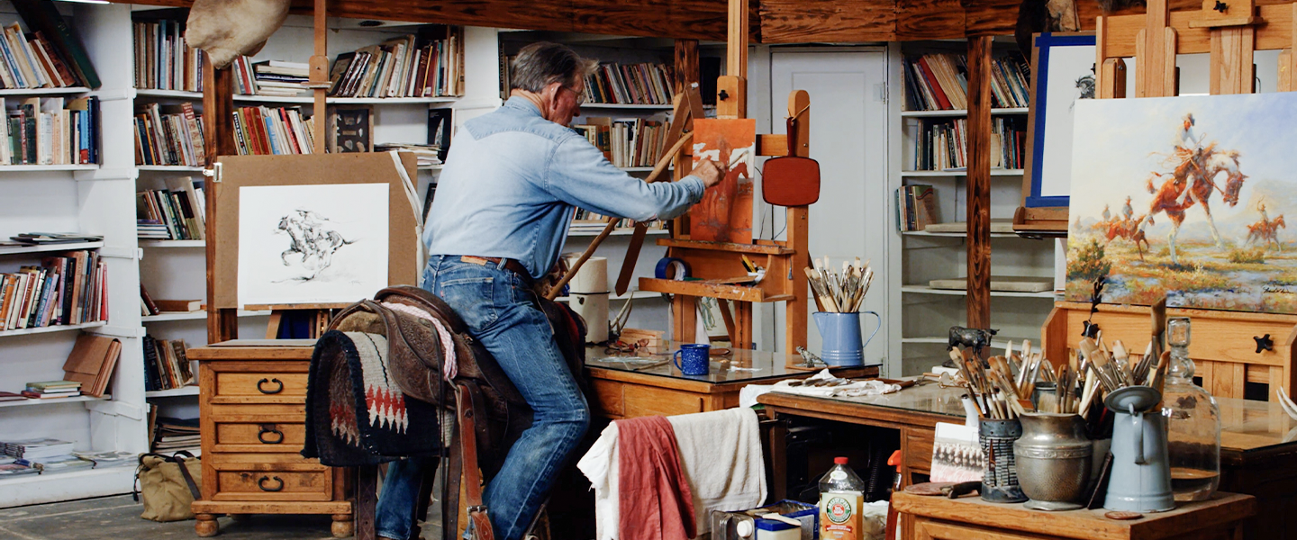 Mike sitting on saddle in studio, painting 